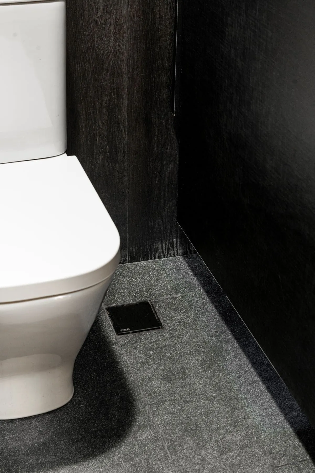 Rejilla de piso Atrim instalada en baño moderno con revestimiento oscuro e inodoro blanco